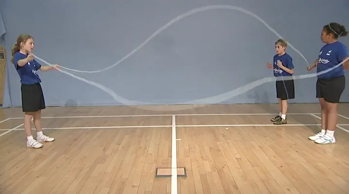 Two pupils turn Double Dutch ropes for a skipper in a sports hall