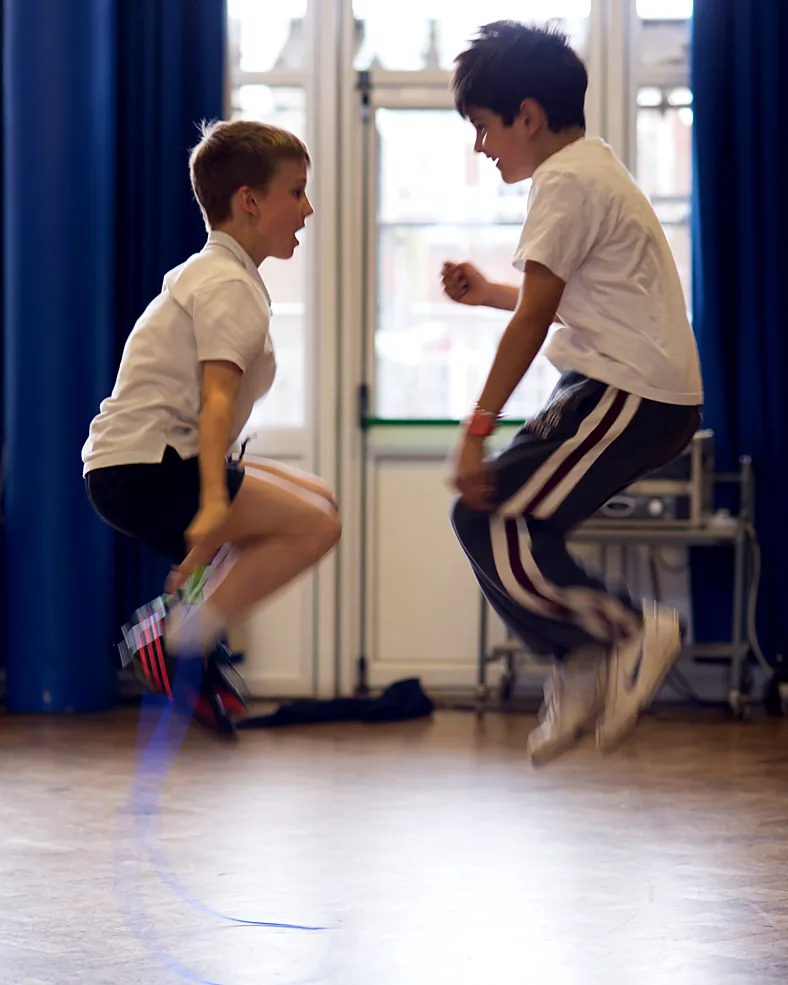 Two primary school boys skipping in a school hall