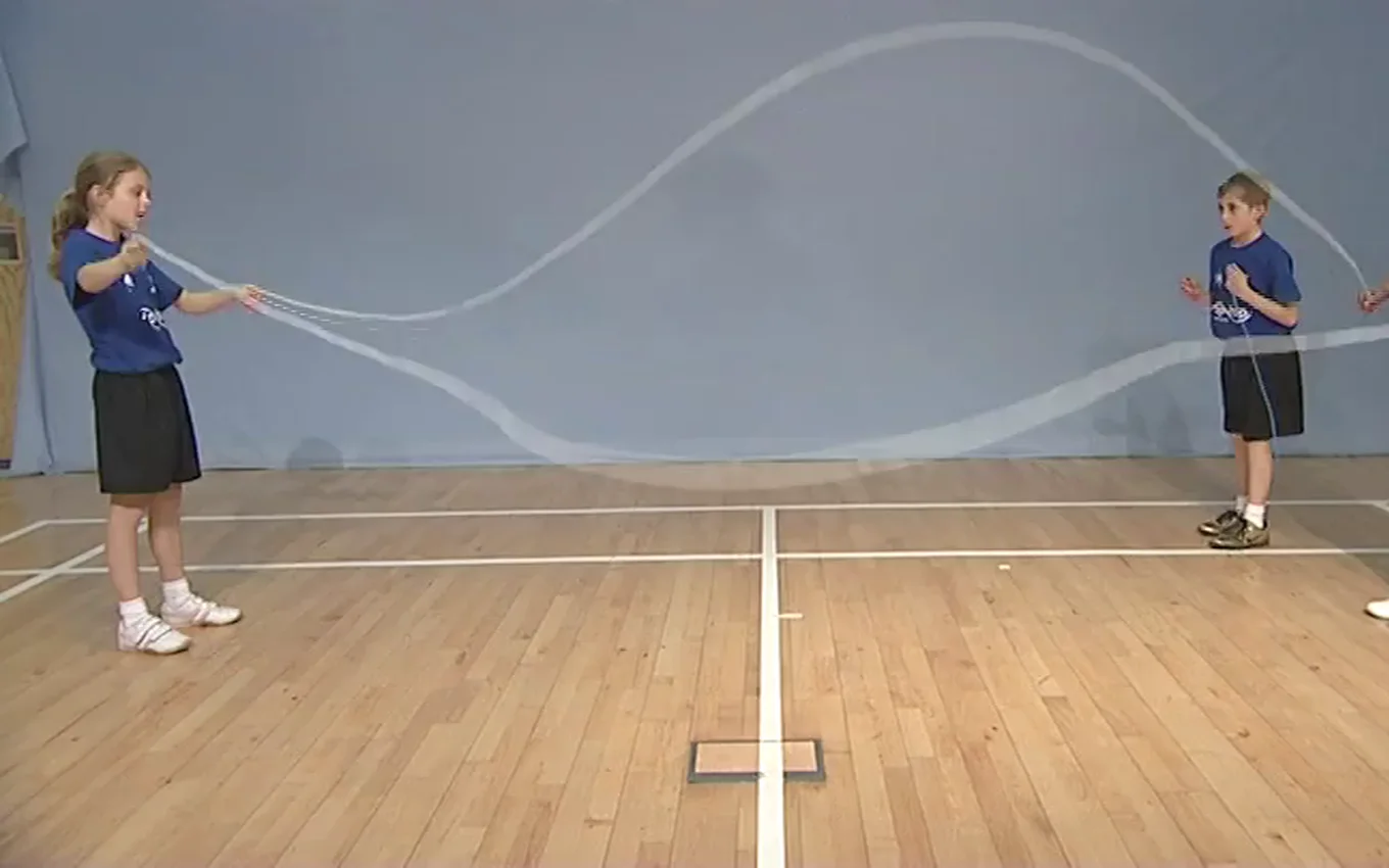Two pupils turn Double Dutch ropes for a skipper in a sports hall